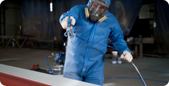 Worker in blue protective suit using a spray gun to apply coating