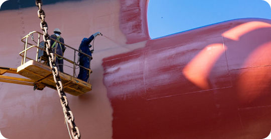 Two workers spraying the hull of a ship using a crane