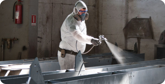 Worker using a spray gun to apply protective coating on metal beams