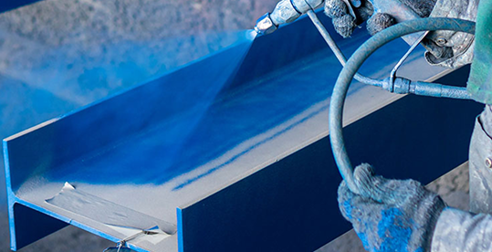 Worker spraying blue protective coating on a metal beam