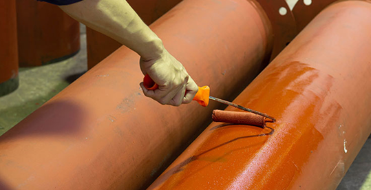 Worker painting an industrial pipe with protective coating