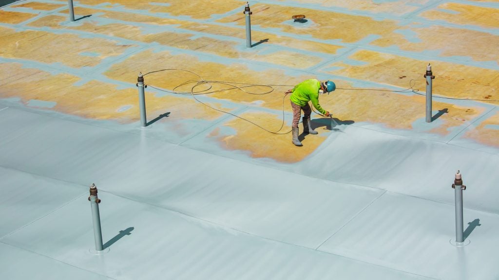 Worker on a roof spraying protective coating with a spray gun