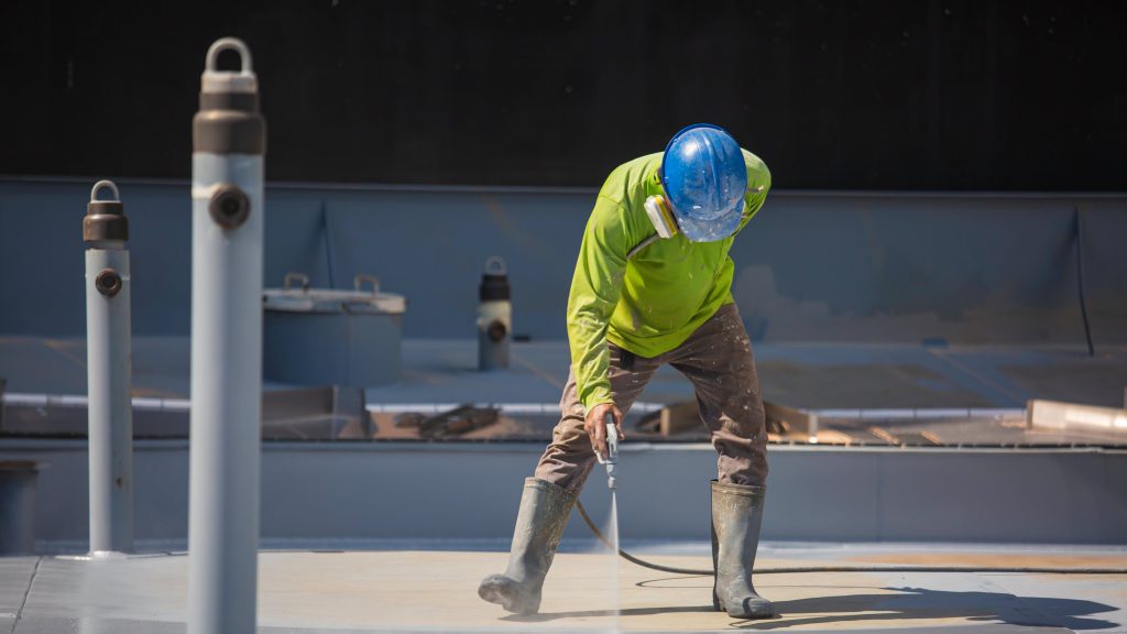 Worker on a roof wearing a safety mask and using a spray gun