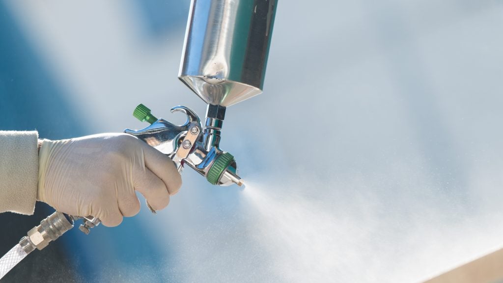 Close-up of worker’s hand using a spray gun to apply corrosion protection coating