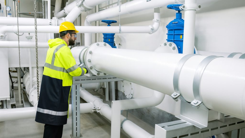 Man in yellow hi-vis jacket and helmet standing in front of pipes coated with intumescent fire-protection coatings