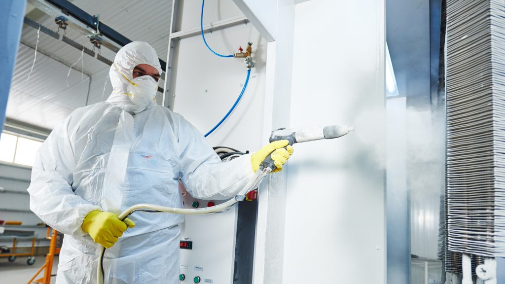Worker in white protective suit spraying high-performance coating on metal surface